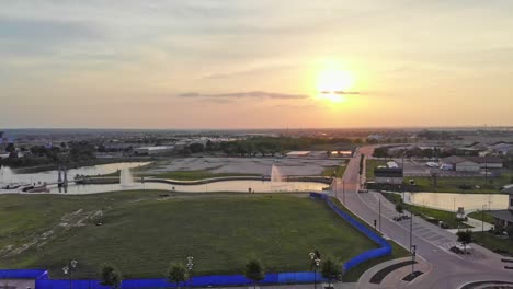 Starting-near-city-hall,-moving-across-yet-to-be-developed-lot,-a-green-field-with-sunset-and-three-large-fountains-near-a-developing-downtown-shopping-and-restaurant-district