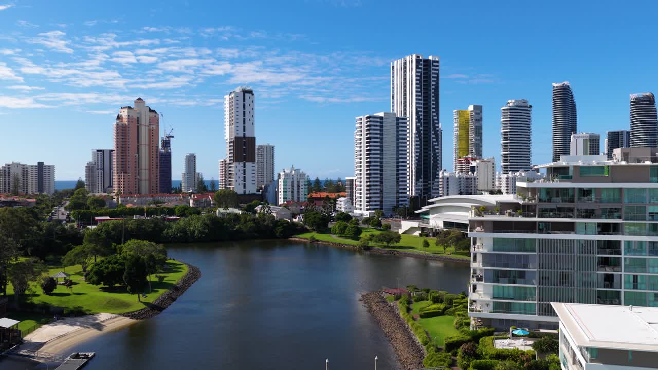 Aerial footage captures Gold Coast's skyline with modern skyscrapers and a serene waterway under clear blue skies