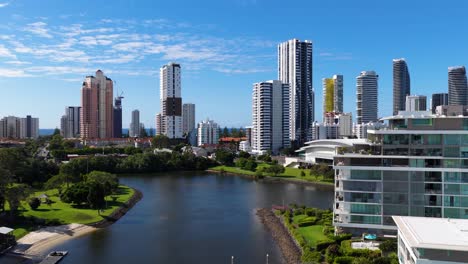 aerial footage captures gold coast's skyline with modern skyscrapers and a serene waterway under clear blue skies