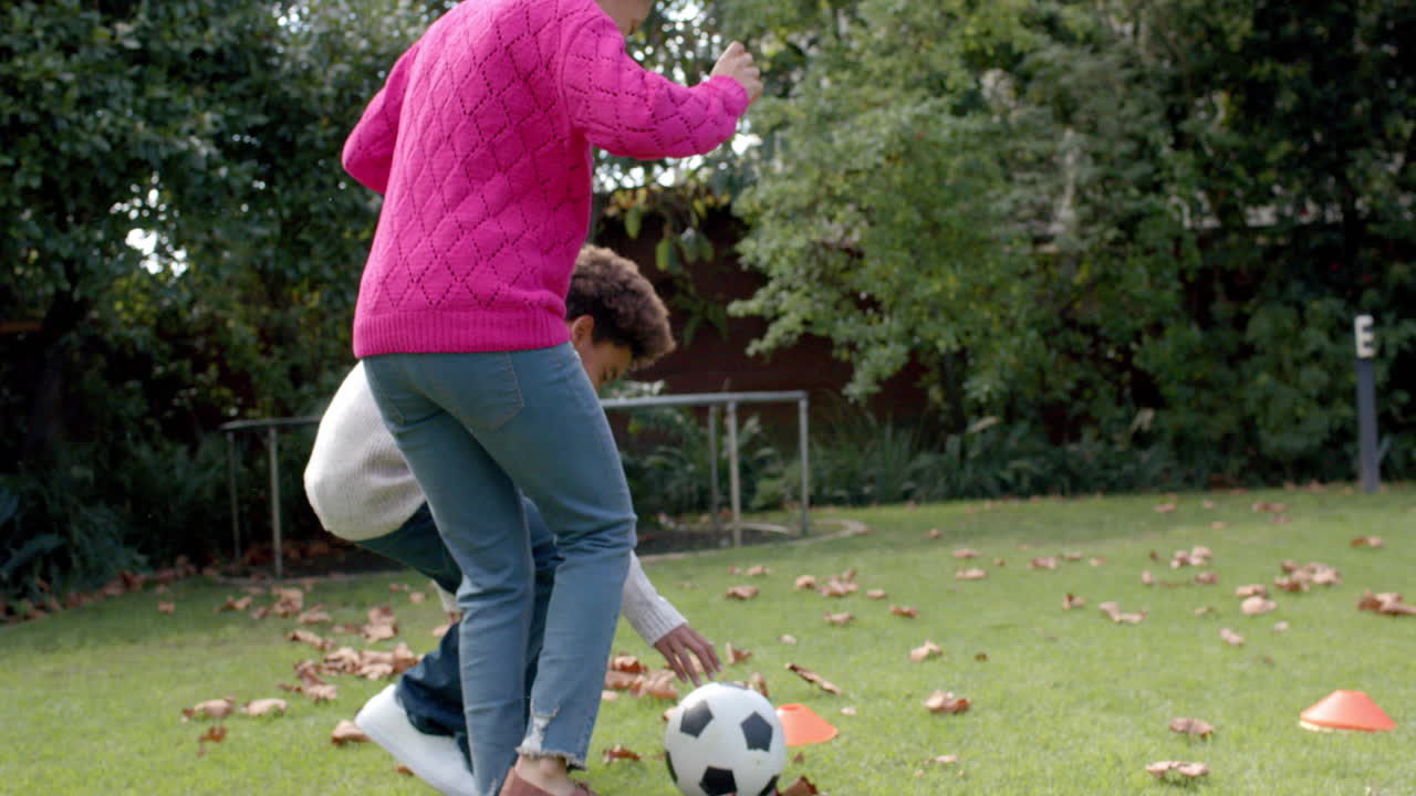 Happy african american mother and son playing football and embracing in garden, in slow motion