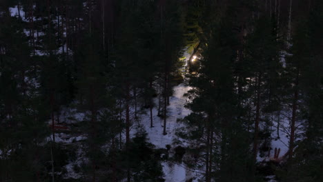 telephoto night drone shot of tree harvester navigating snowy track in forest