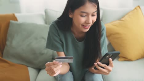 joven asiática feliz con tarjeta de crédito usando pagos móviles instantáneos en casa. mujer cliente sonriente haciendo compras en teléfono inteligente recibiendo concepto de devolución de dinero.