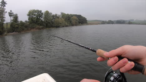 A-fisherman-reels-on-a-Swiss-lake-in-the-canton-of-Vaud,-border-made-of-trees