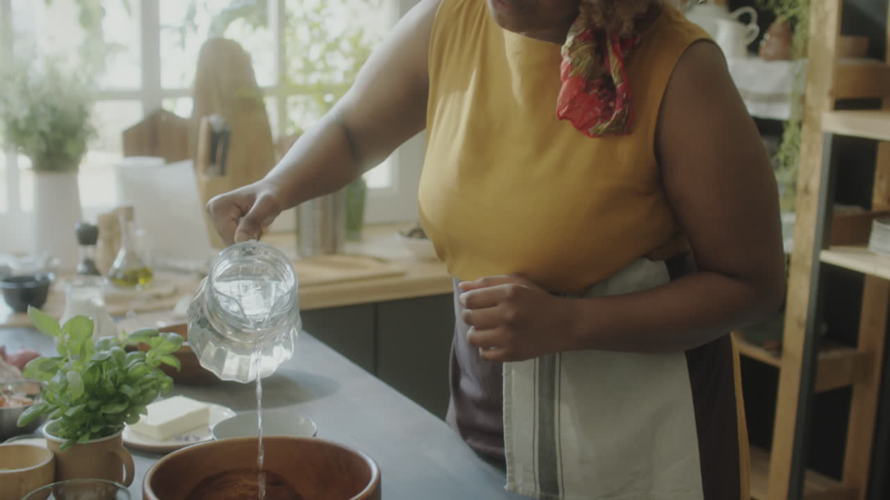 African American Woman Adding Water to Bowl while Cooking