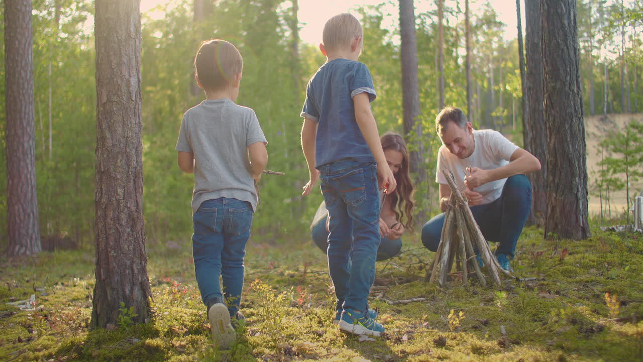 가족은 여름 저녁에 캠프 불 주위에 앉아 있습니다. 아이들은 부모와 함께 숲에서 휴식을 취하고 있습니다. 좋은 회사에서 자연에서 주말. 가족은 숲에서 불에 소시지를  ⁇ 고 있습니다.
