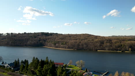 Ascending-aerial-shot-of-natural-lake-with-cottage-and-forest-in-background-during-sunset