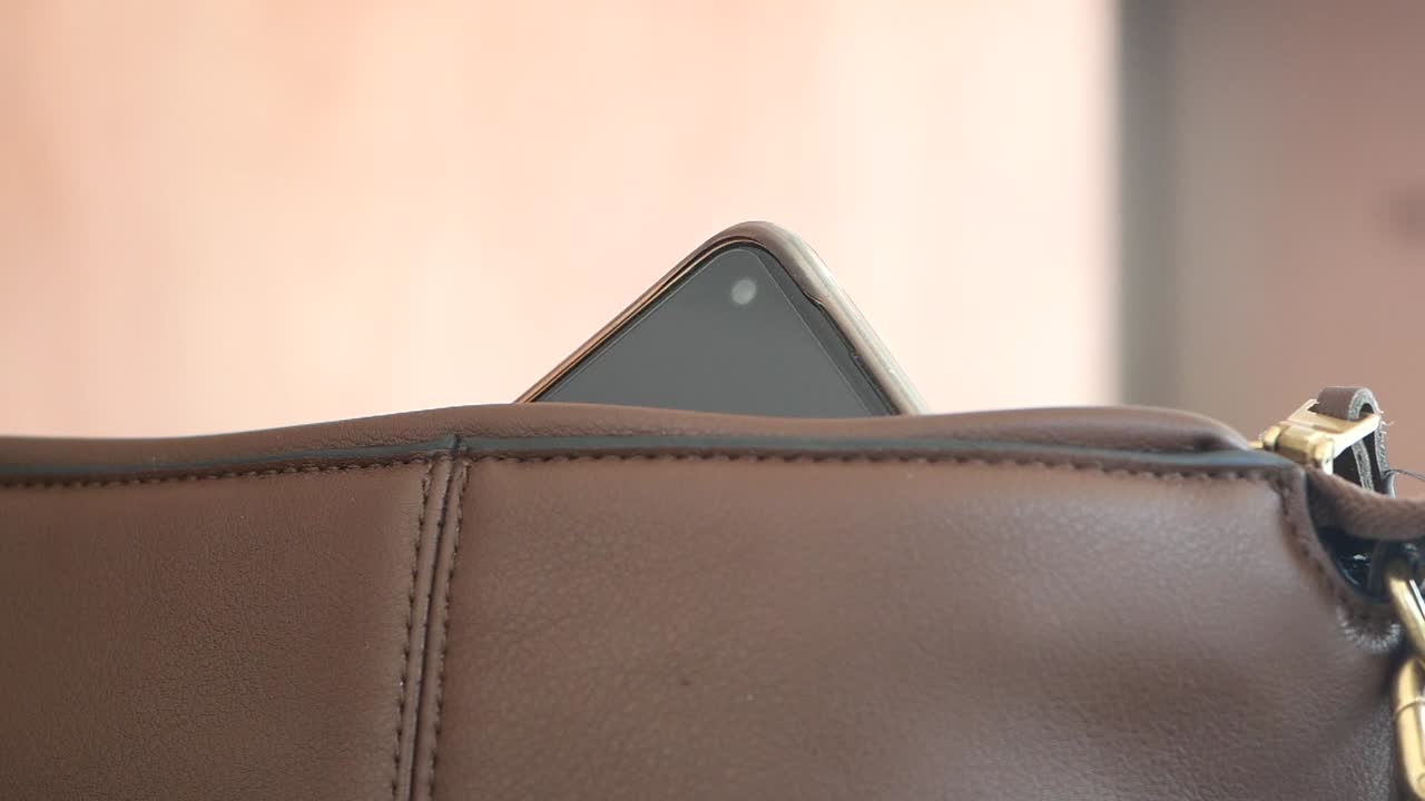 una mano sosteniendo un teléfono, poniéndolo en una bolsa marrón