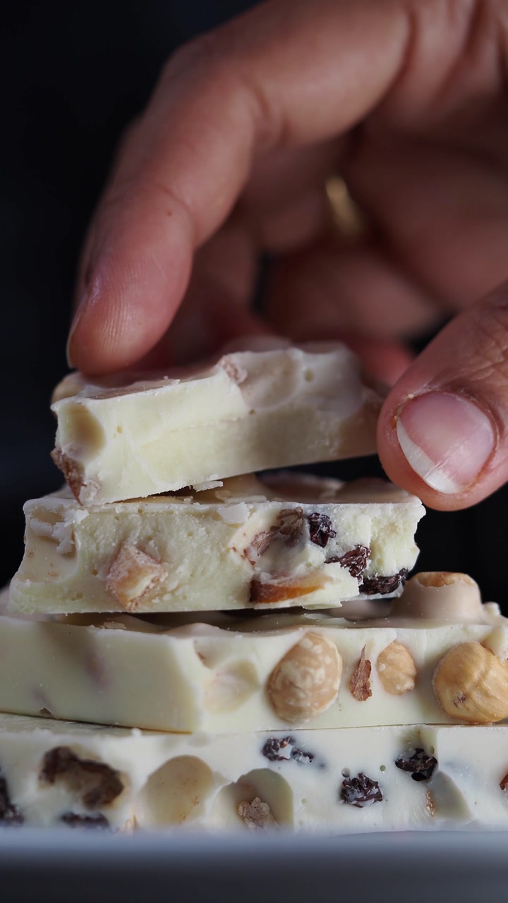 Hand Picking Up a Piece of White Chocolate Bark with Hazelnuts and Dried Fruits