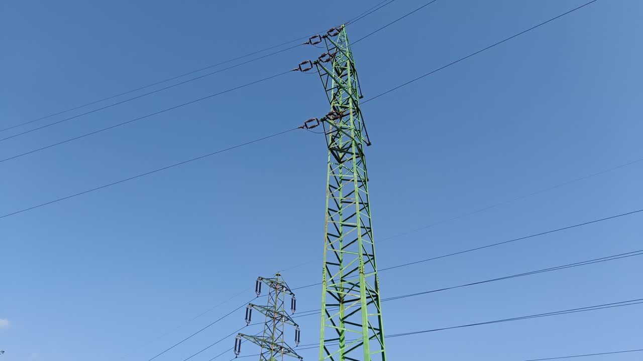 Panning shot revealing green electric pylon with high-voltage wires to transmit electricity on long distances