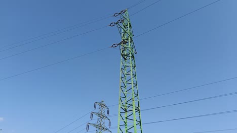 toma panorámica que revela un pilón eléctrico verde con cables de alto voltaje para transmitir electricidad a largas distancias