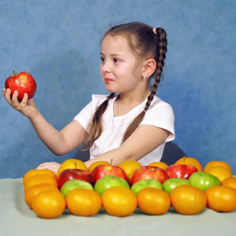 little girl eating apple. delicious fresh fruit are placed nicely on the table. beautiful child bites juicy apple and offering it to somebody. healthy food.