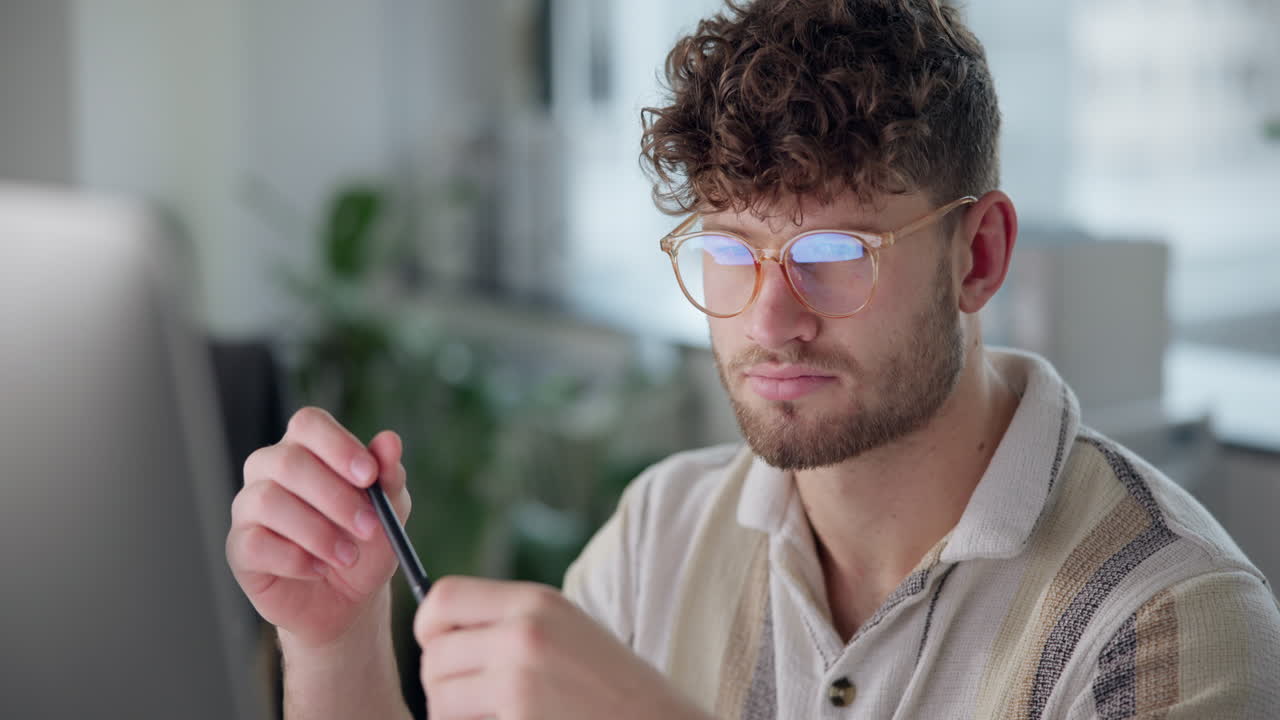 Man with curly hair and glasses holding a pen