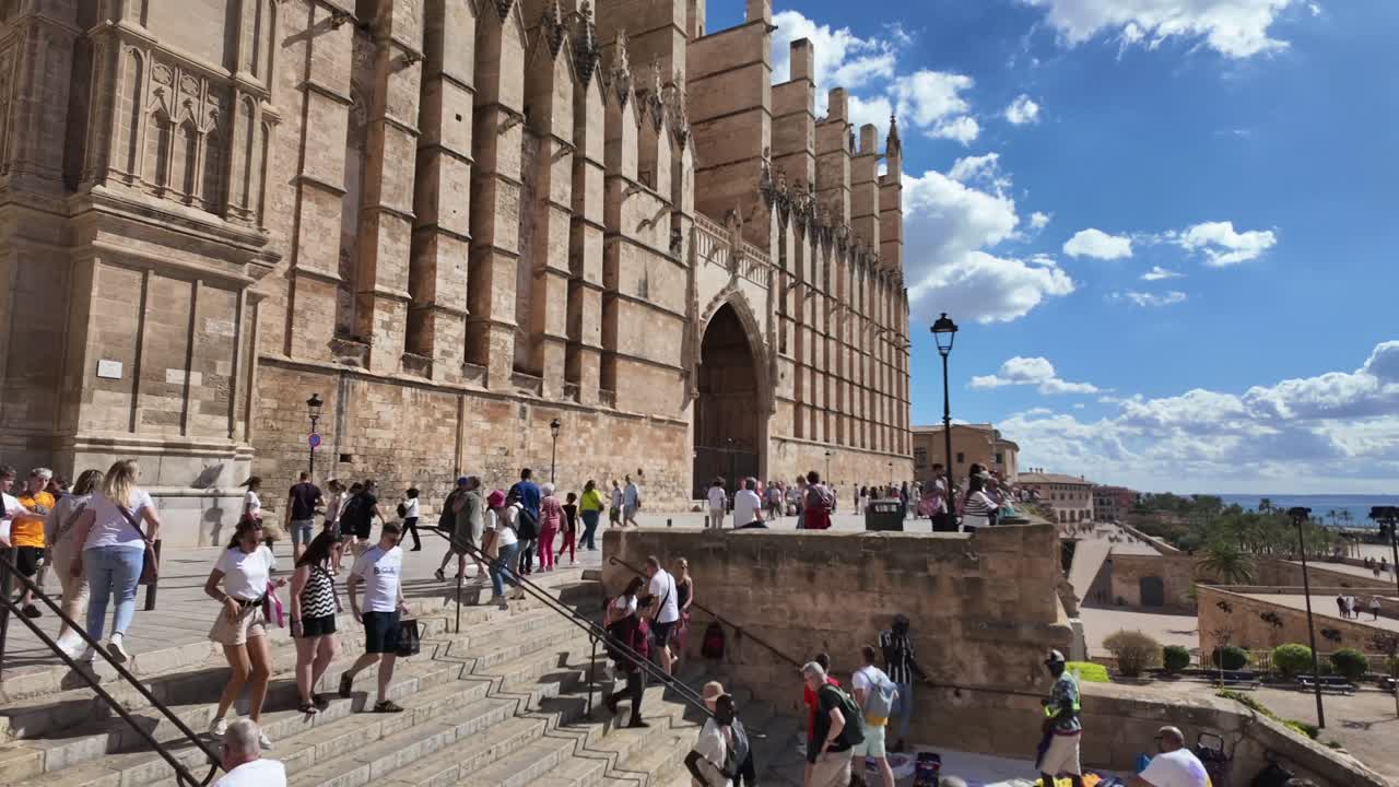 Palma de Mallorca’s Cathedral. Motion lapse left to right in a sunny summer morning with some clouds in the sky and visitors coming and going. 4K
