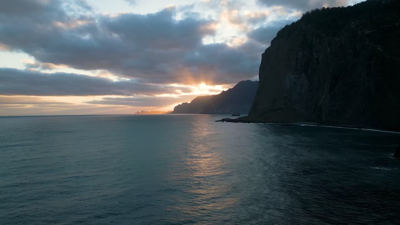 imágenes de drones volando sobre el mar en madeira con montañas en el fondo y un hermoso amanecer rompiendo a través de las nubes