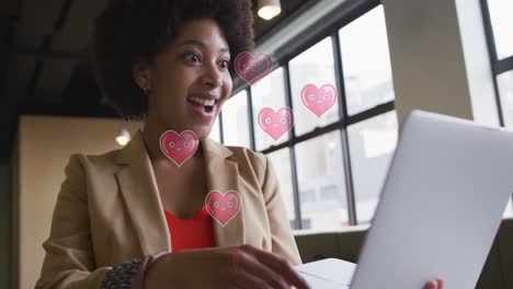 Animation-of-hearts-falling-over-african-american-woman-using-laptop