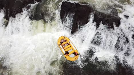 Vista-Aérea-De-Drones-De-Un-Bote-De-Rafting-Amarillo-Que-Intenta-Descender-Por-Una-Cascada-En-El-Río-Nilo-En-Jinja,-Uganda