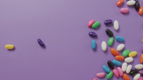Video-of-overhead-view-of-multi-coloured-sweets-falling-over-purple-background