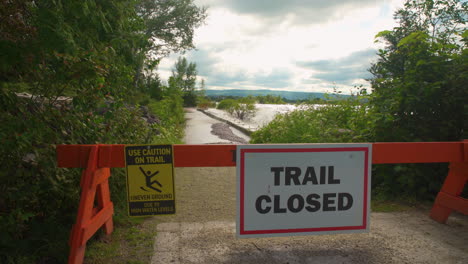 waves crashing into a bulwark behind a sign that reads "trail closed