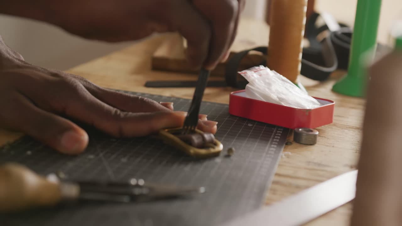 Hands of african american craftsman preparing belt in leather workshop