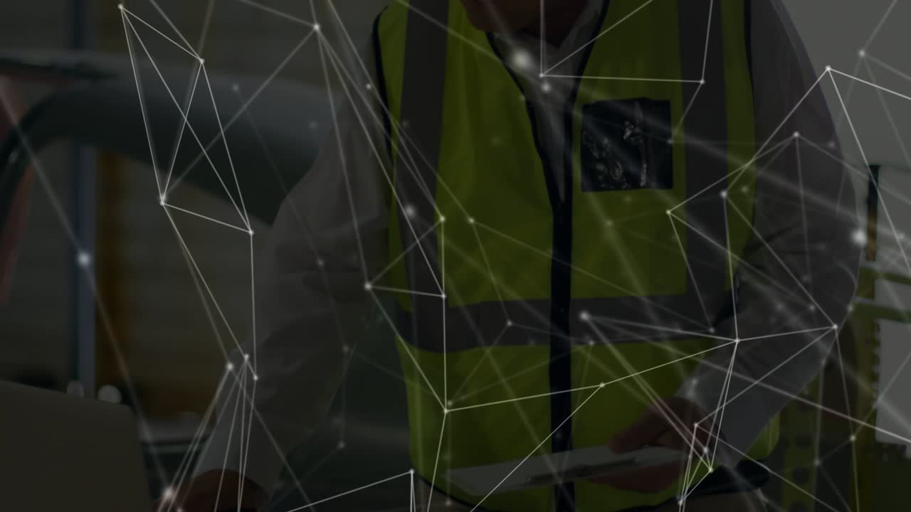 Uomo anziano con giubbotto ad alta visibilità che esamina i piani, usa un tablet e un laptop in officina con connessione di rete