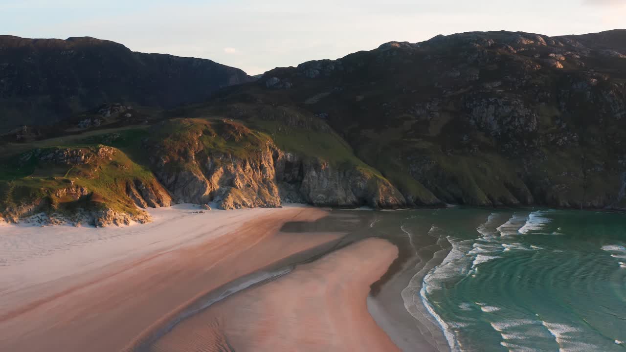 Aerial Orbit of Maghera Beach with Mountainous Backdrop During Sunset With Waves Gently Receding Into the Shore