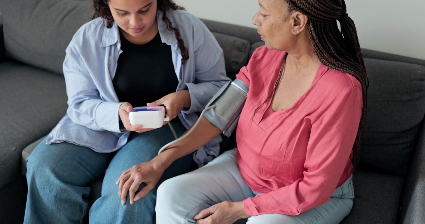 Young Woman Helping Senior Woman Measure Blood Pressure at Home