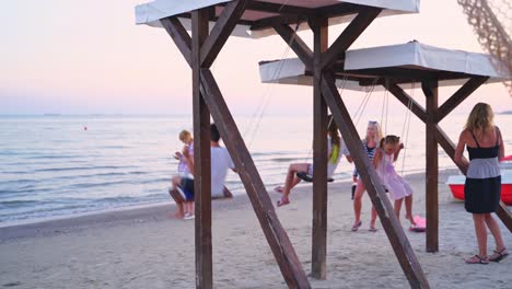 back side view of children swinging on the sea background. boy and girl on a wooden swing having great time near the evening sea.