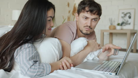 couple relaxing in bed using a laptop