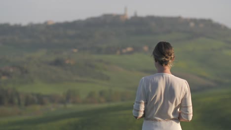 Young-woman-dressed-in-white-calmy-standing-in-Tuscan-field,-wind-gently-blows
