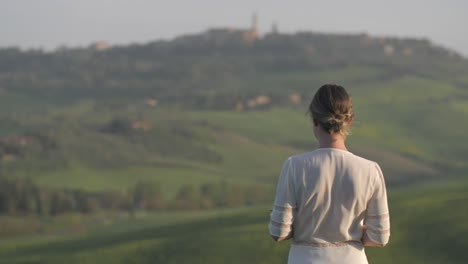 junge frau in weiß gekleidet steht ruhig auf toskanischem feld, wind weht sanft