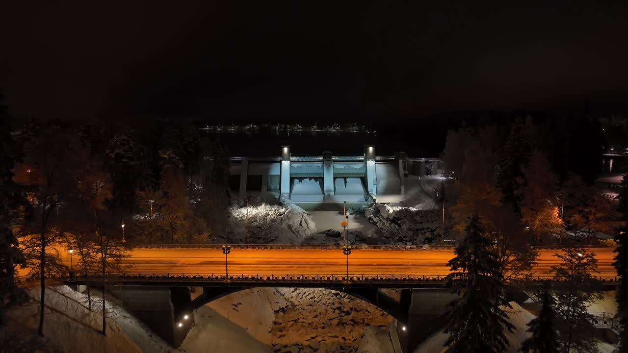 Drone approaching the illuminated Imatrankoski dam, winter night in Finland