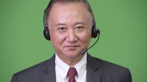 mature japanese businessman working as call center representative against green background