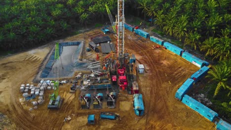 Cinematic-4K-Drone-Footage-of-Onshore-Drilling-Rig-equipment-structure-for-oil-exploration-and-exploitation-in-the-middle-of-jungle-surrounded-by-palm-oil-trees-during-sunset-and-high-oil-price