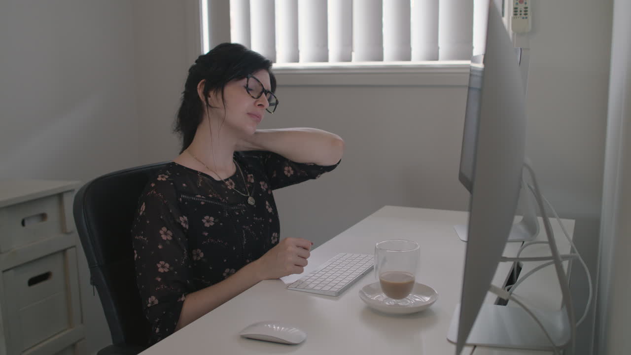 Professionally dressed woman rubbing sore neck while trying to work from home