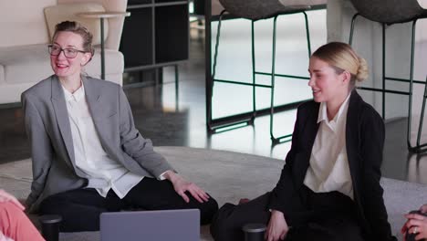 A-group-of-confident-blonde-Business-Women-in-business-suits-sit-on-the-carpet-in-the-office-and-communicate-during-their-break-at-work