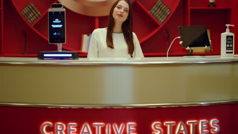 woman posing camera at reception. receptionist waiting guests signboard counter