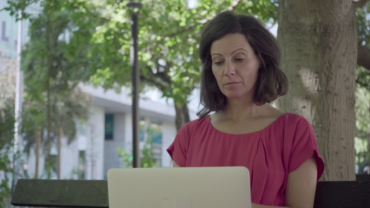 mujer de mediana edad pensativa usando una computadora portátil en el parque de verano.