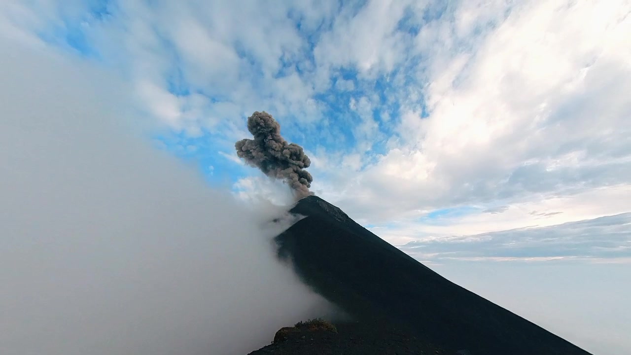 Video eines Ausbruchs des Vulkans Fuego in Guatemala mit Wolken auf der einen Seite und Asche, die aus der Bergspitze austritt