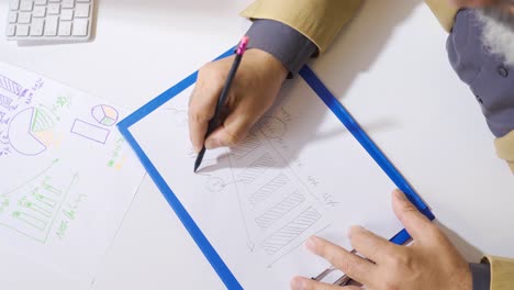 male hand in suit drawing financial statement on paper on office desk.