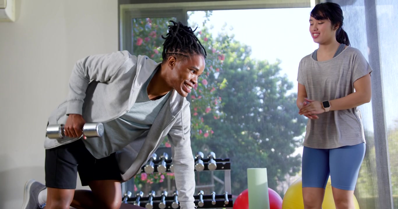 Afrikanischer Trainee folgt Anweisungen des asiatischen Trainers, nimmt Hantel auf und führt Ruderübungen im Fitnessstudio korrekt aus.