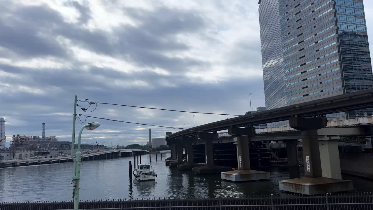 A train travels over a river in Tokyo, Japan, with a tall building and cloudy sky