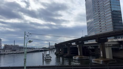 a train travels over a river in tokyo, japan, with a tall building and cloudy sky