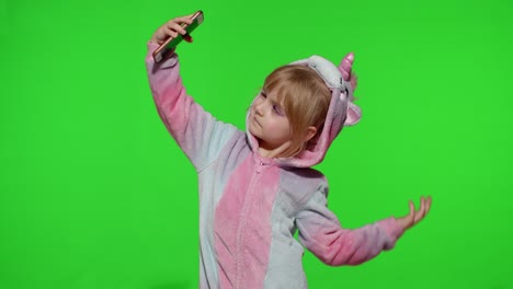 Child-girl-in-unicorn-costume-pajamas-using-smartphone,-kid-emotionally-makes-selfie-on-mobile-phone