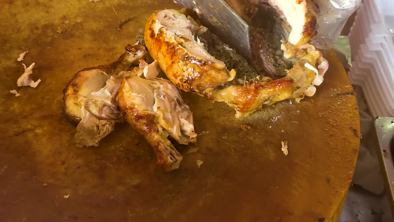 Close-up of roasted chicken being sliced on a wooden board, with plastic containers nearby.