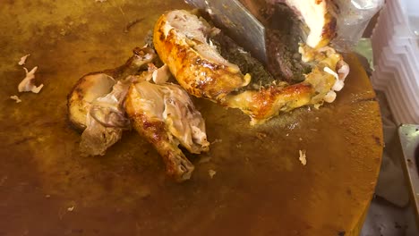 close-up of roasted chicken being sliced on a wooden board, with plastic containers nearby.