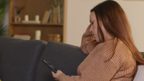 woman sitting on sofa at home using mobile phone to check social media message and scrolling online 14