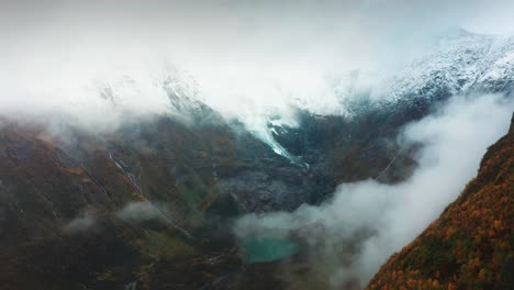 a fog-covered glacier descends through the mountain, with water trickling from its edges amid fall colors