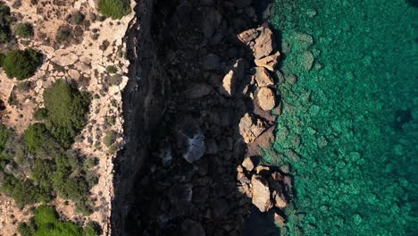 Broken-cliff-and-crystal-clear-water-sparkling-top-down-drone-shot