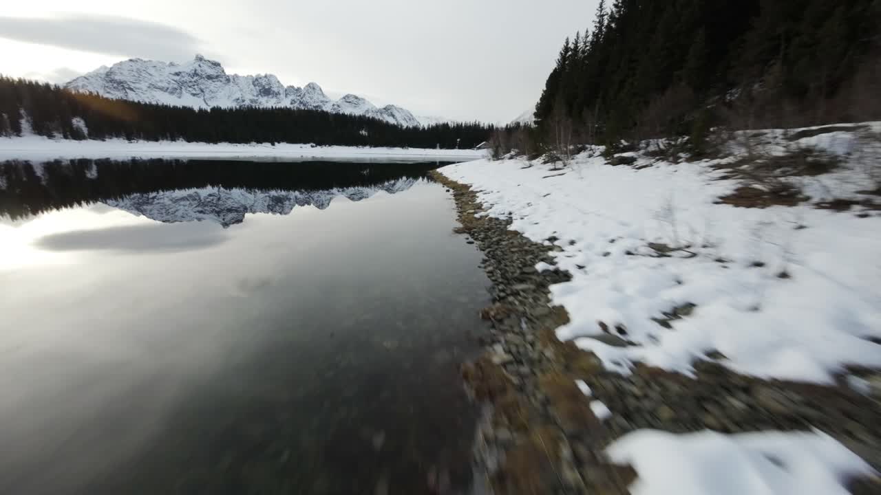 Montagne italiane innevate riflesse in un lago alpino, ripresa veloce con drone FPV.