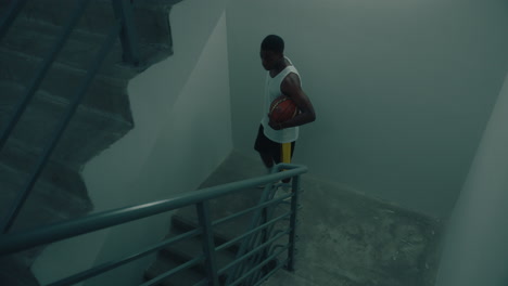 black basketball athlete walking downstairs with ball in apartment building
